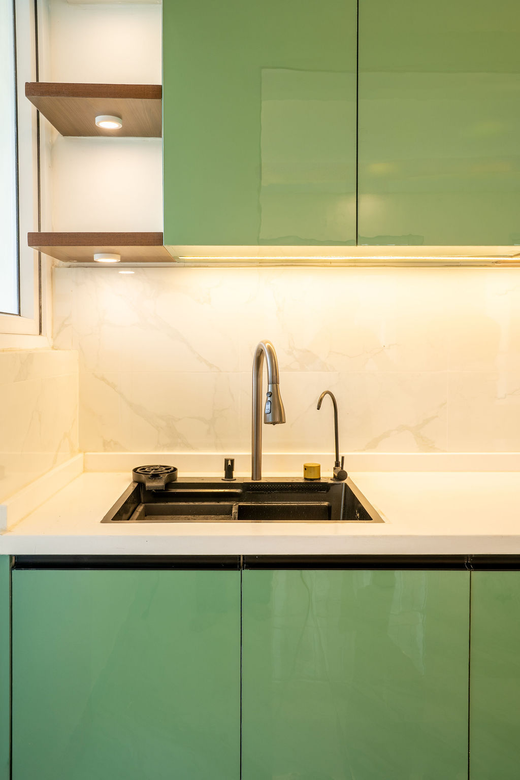 Pista-green kitchen sink corner with marble backsplash and lit wooden shelves