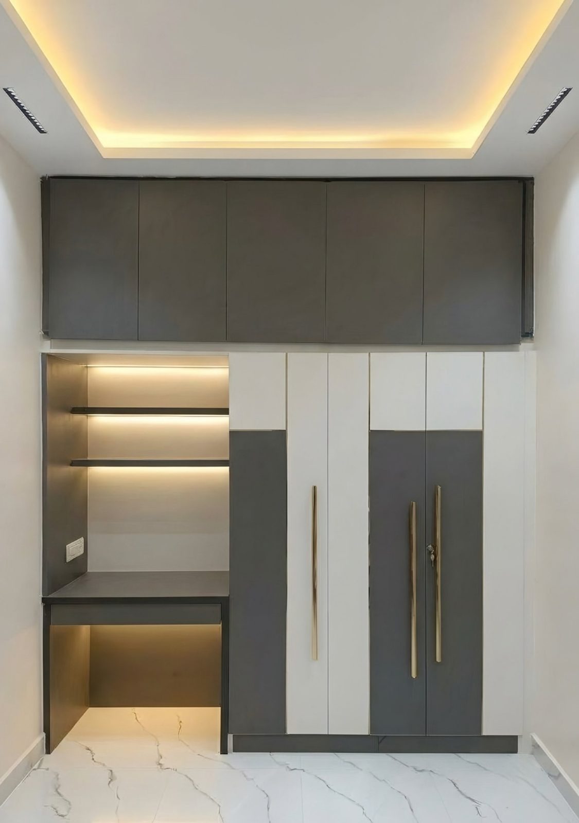 Grey and white bedroom wardrobe with gold handles and a built-in backlit study desk, 2 BHK interior in Hassan